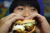 A boy poses with a chicken burger at a fast food outlet