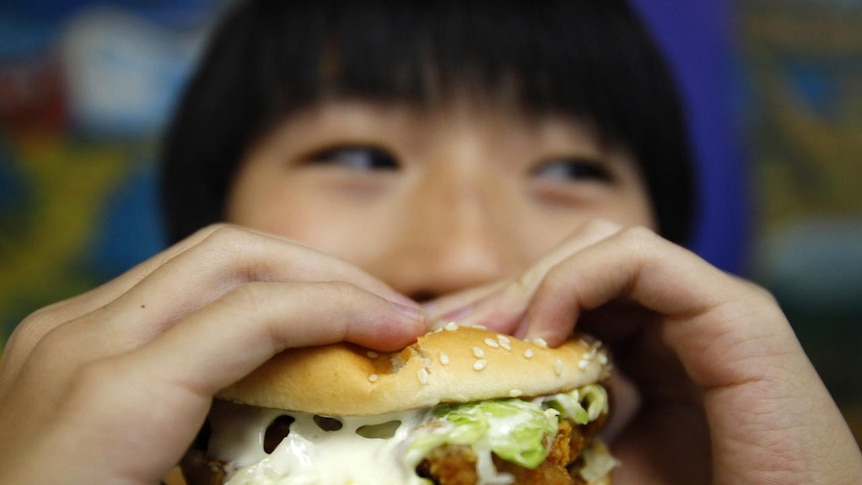 A boy poses with a chicken burger at a fast food outlet