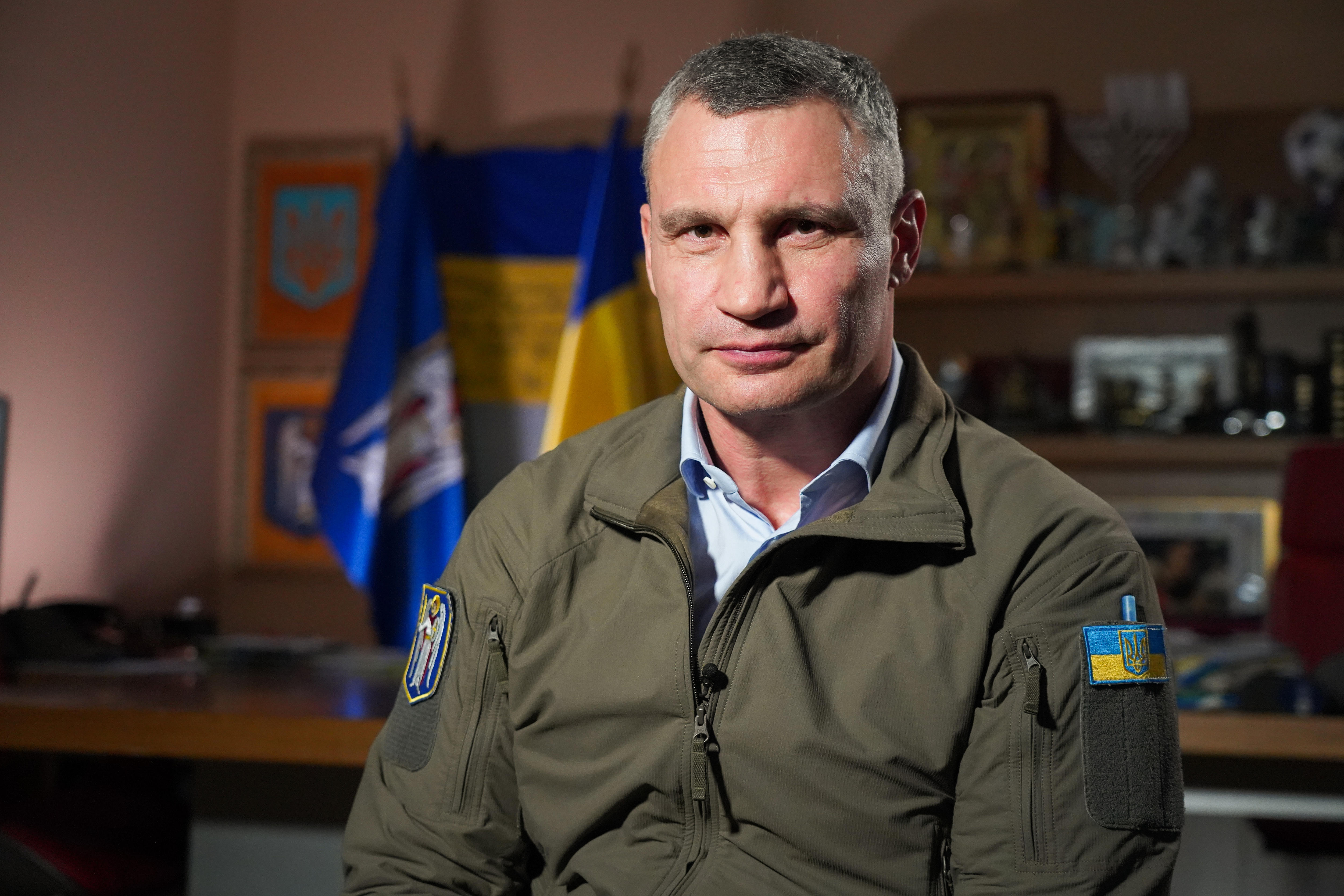 A man with grey hair smiles while wearing a kharki jacket.