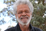 A head and shoulders shot of an older Indigenous man with grey hair posing for a photo outdoors.