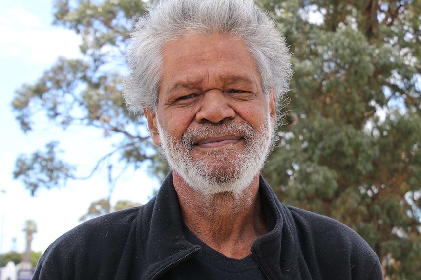 A head and shoulders shot of an older Indigenous man with grey hair posing for a photo outdoors.