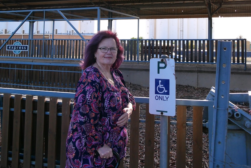 A lady in a purple dress with a purple dress standing in front of a disabled park with her walking stick