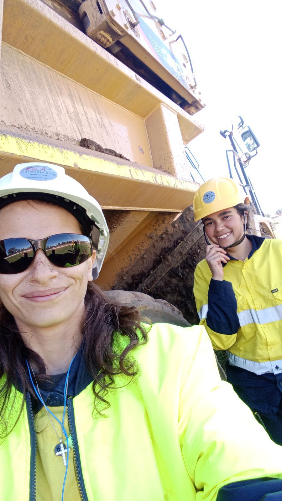 Two women in high vis wearing hard helmets stand next to a tractor.