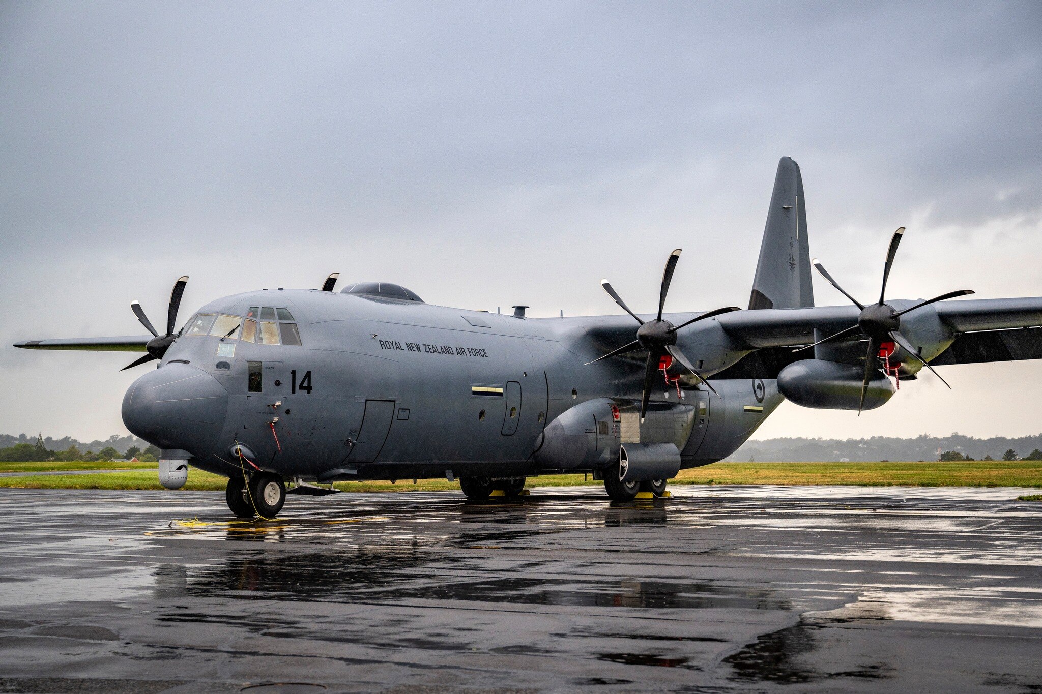 A large grey C-130J-30 plane on a wet tarmac.
