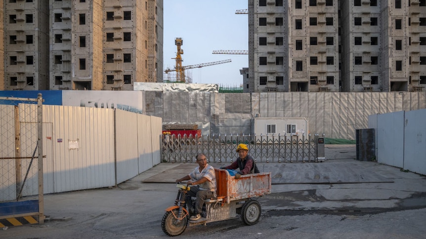 Two people on a tricycle ride past an uncompleted building site in Beijing, China.