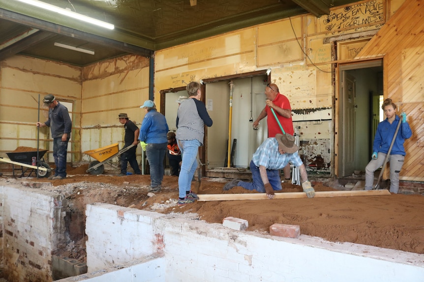 A group of people with shovels, wheelbarrows and wood working inside a building site.