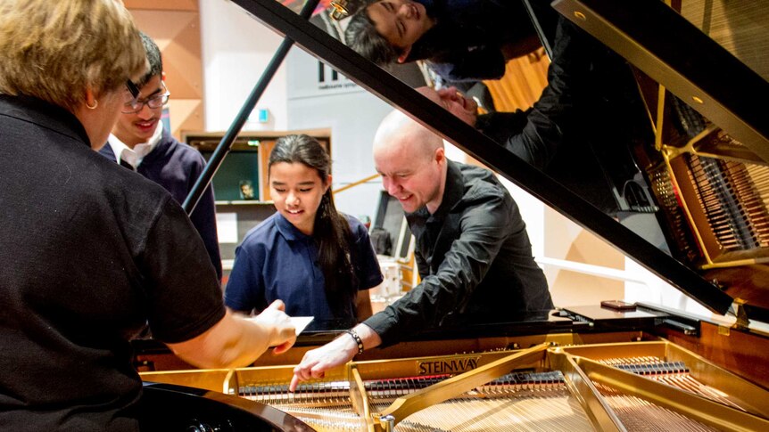 Students in school uniform look at a Steinway grand piano with a man dressed in black.