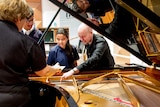 Students in school uniform look at a Steinway grand piano with a man dressed in black.