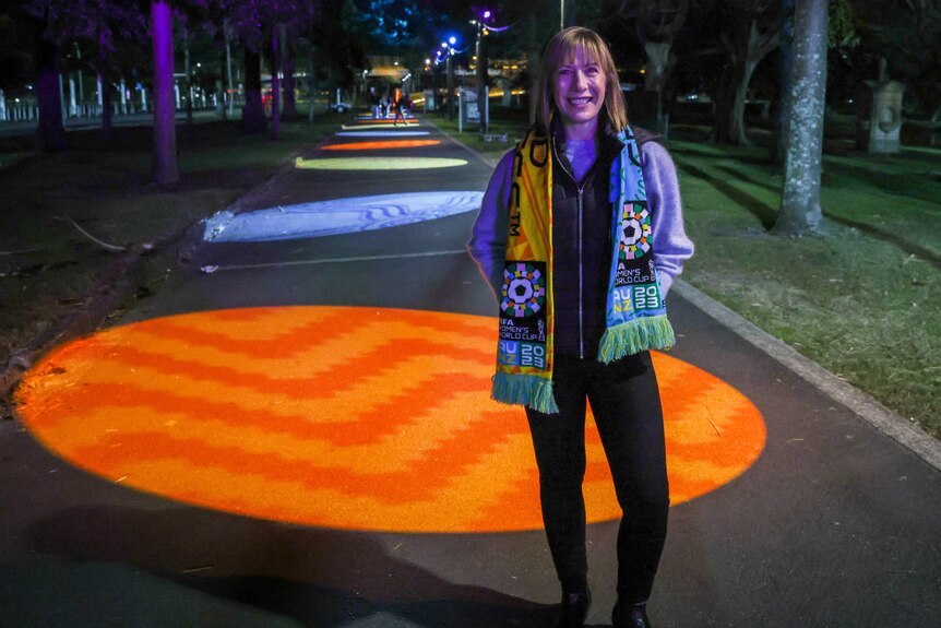 a woman standing outdoors at a park with a round light illuminating the path
