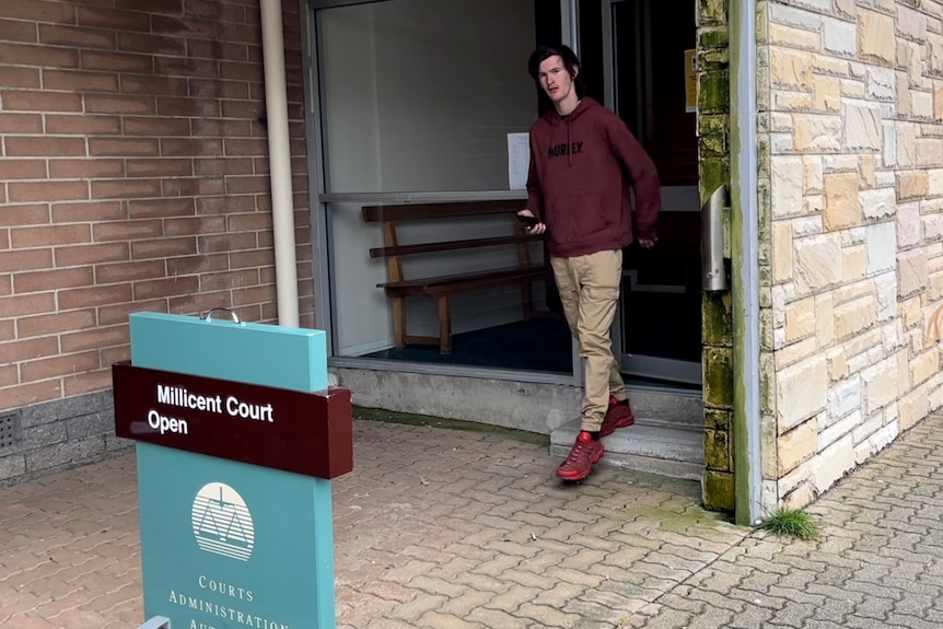 A young man with dark hair exits a court building.