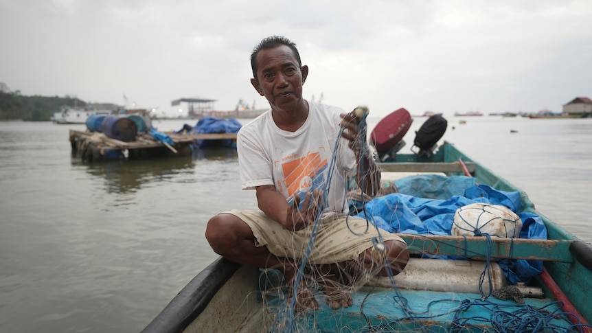 A man on a small fishing boat holds a fishing net. 