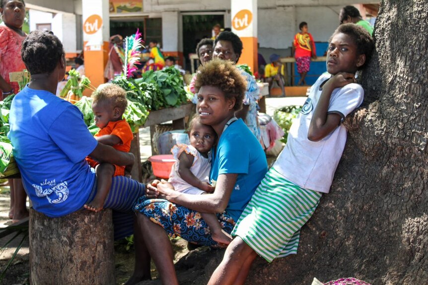 A group of people gather outside a market on an island in Vanuatu.