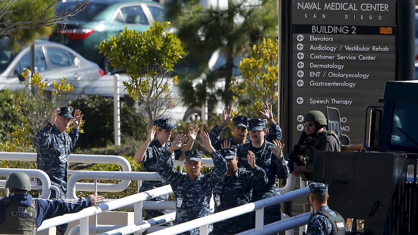 Navy personnel leave building with hands up.
