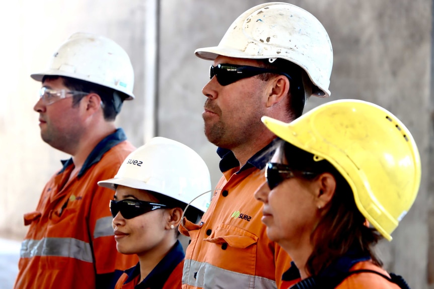 Four workers in high vis vests and hard hats stand in a row