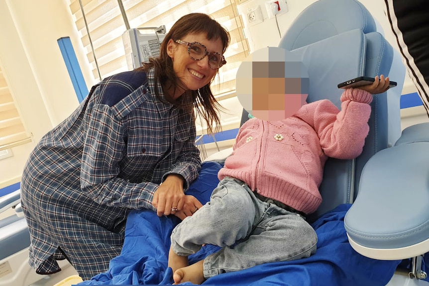 Rachel Coghlan smiles as she stands close to a five-year-old girl (face blurred) in a hospital bed in Gaa. 