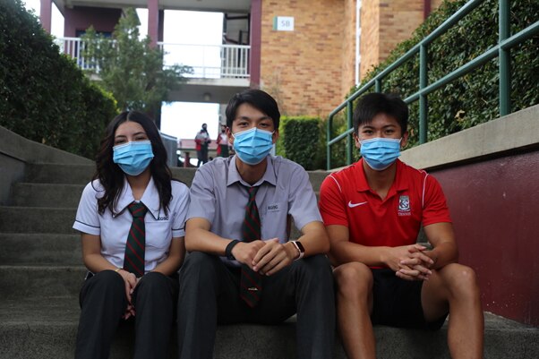An image of three students sitting on step at school with masks on