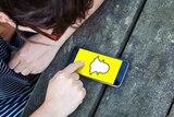 A teenager looks down at a smartphone screen displaying the Snapchat logo, a yellow screen with a white ghost cartoon