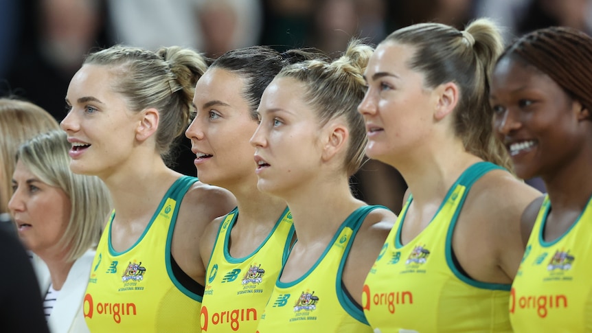 Australian netball players stand in a line and sing with smiles on their faces
