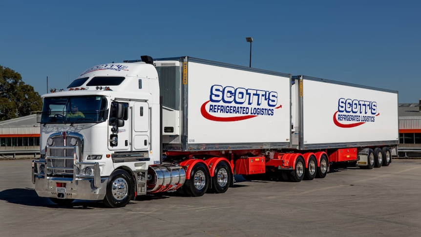 A white truck tows two refrigerated containers. 