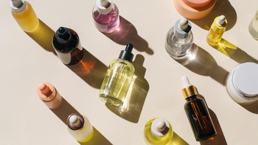 An array of clear dropped bottles of different colours, on cream surface,  taken from above