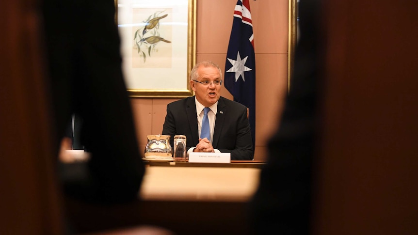 PM pictured between to chairs, sitting in front of a flag.