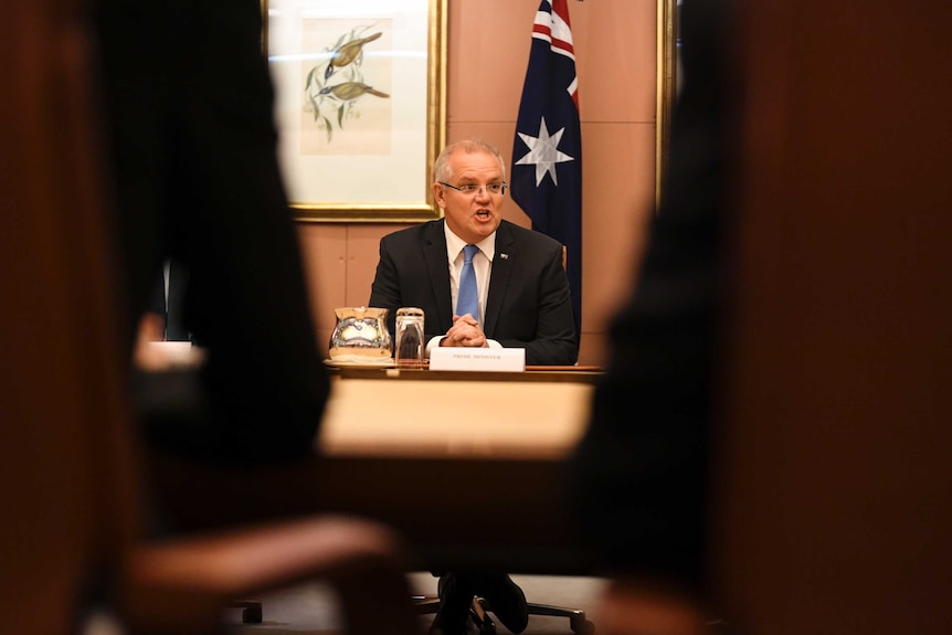 PM pictured between to chairs, sitting in front of a flag.