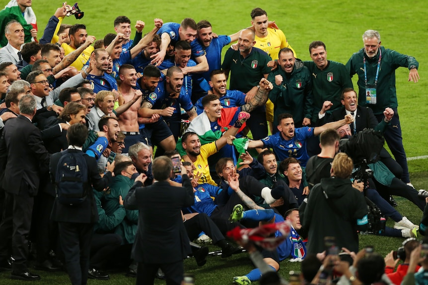 A massive group of Italy players and coaches gather in a pack for a photo in front of the crowd