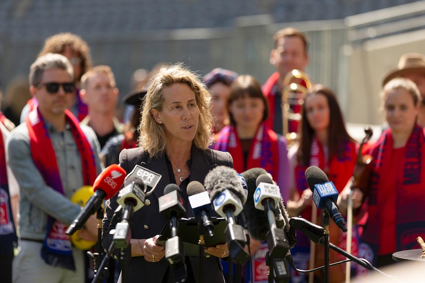A woman speaks with several microphones in front of her
