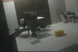 A man shifts a chair and table in front of a door in a grainy video still showing a hospital corridor.