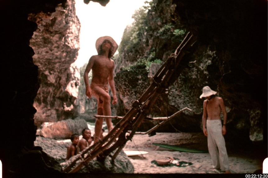 Two men stand in a cave at Uluwatu, while two Balinese boys sit behind them. 