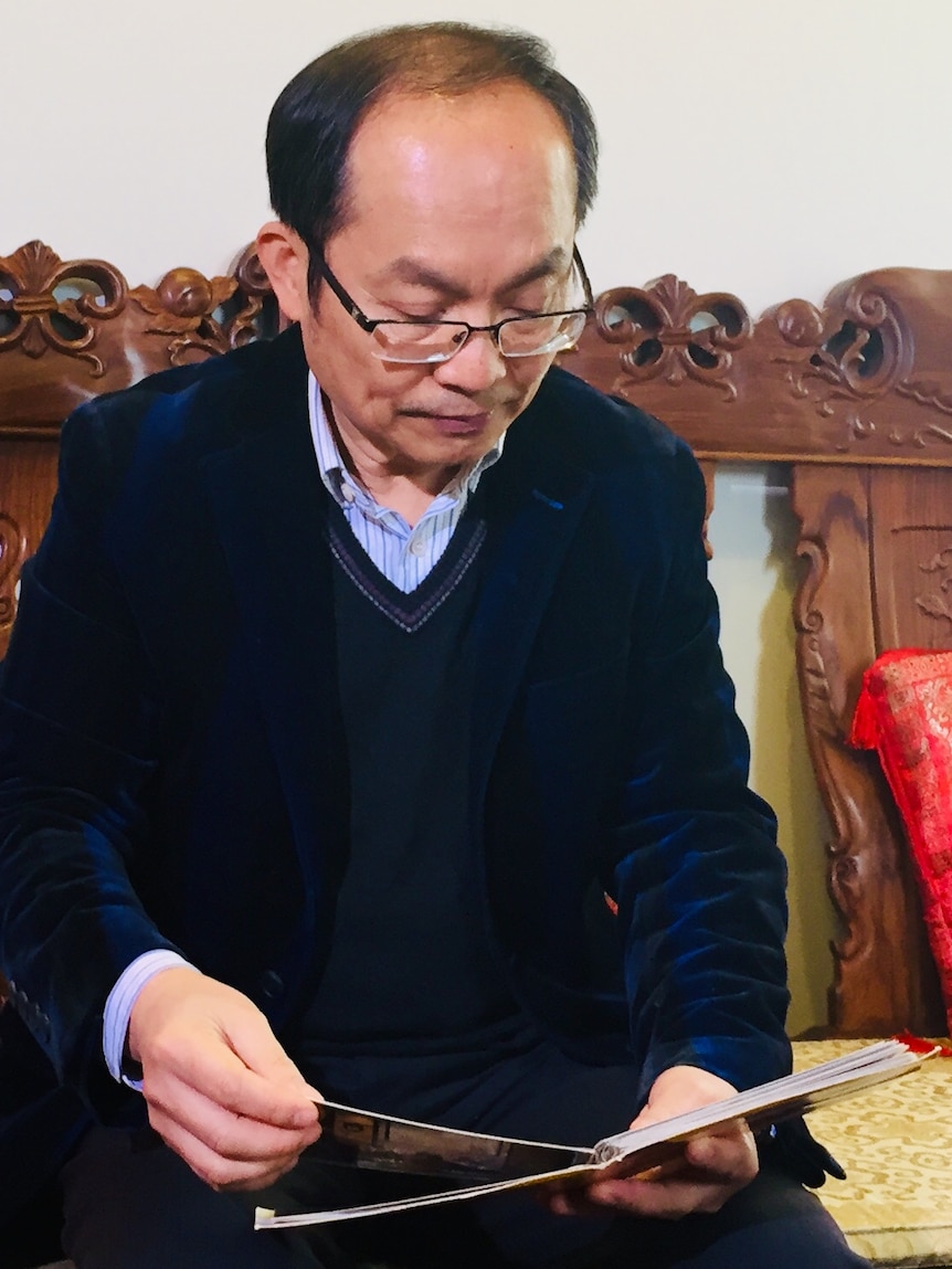 Chongyi Feng at his home looks at a photo album.