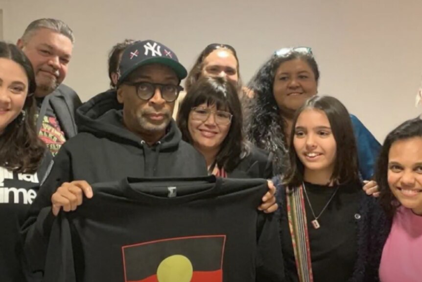 Spike Lee holding a t-shirt with an Aboriginal flag on it. Others in photo include Kara Rose and Miranda Tapsell.