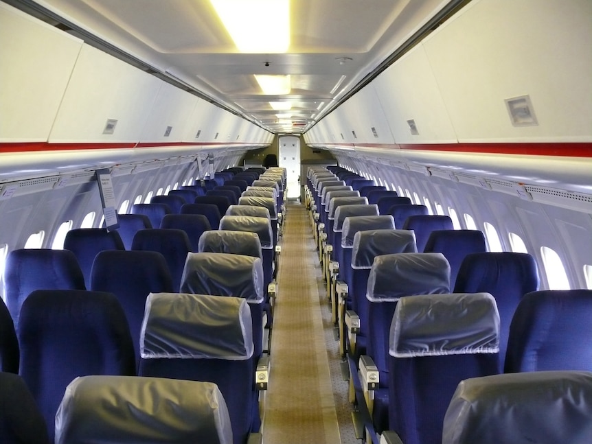 The inside of an airplane cabin on display in a museum shows rows of three seats on one side, an aisle, then two