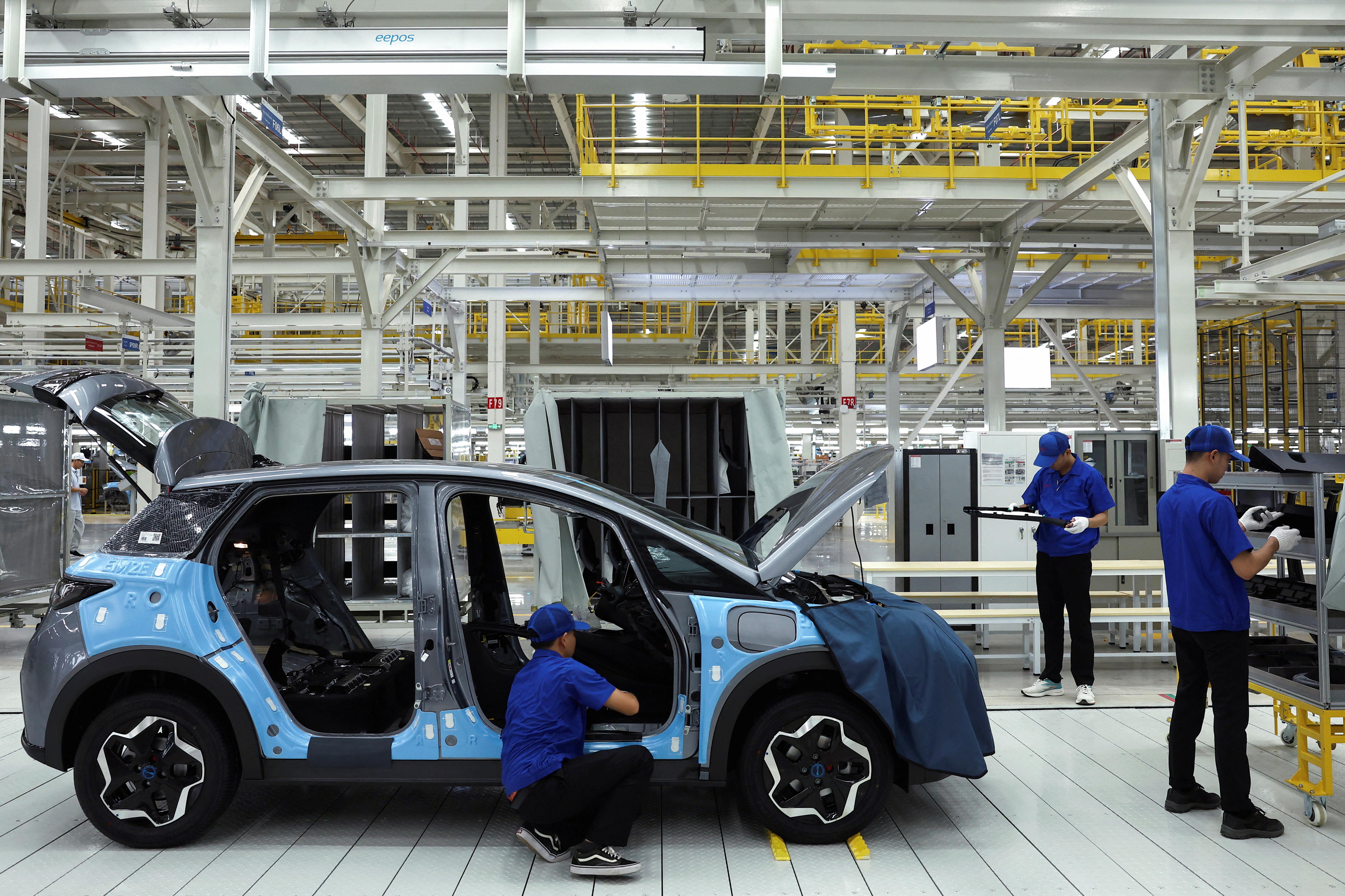 Workers dressed in blue in a factory work on a car. 