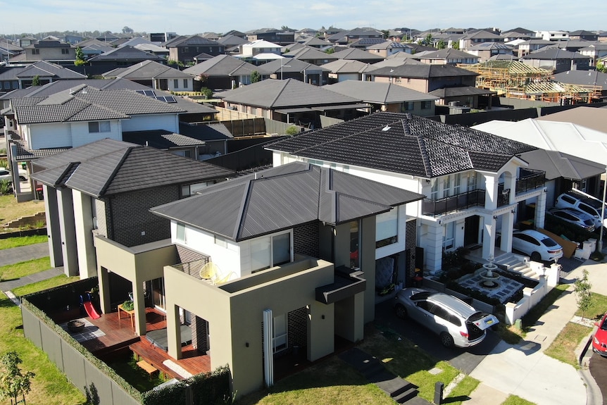 An aerial shot shows a relatively new house in the foreground, with other similar houses behind.