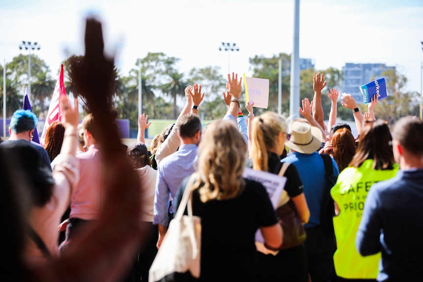 A crowd of teachers stands during a rally at Gloucester Park in Perth with their arms aloft as they took a vote.