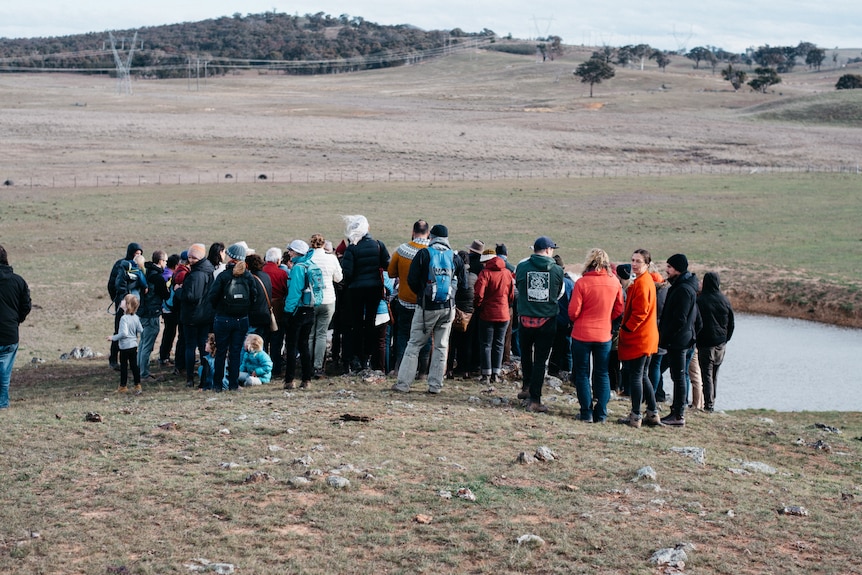 A group of people in a bare paddock. 