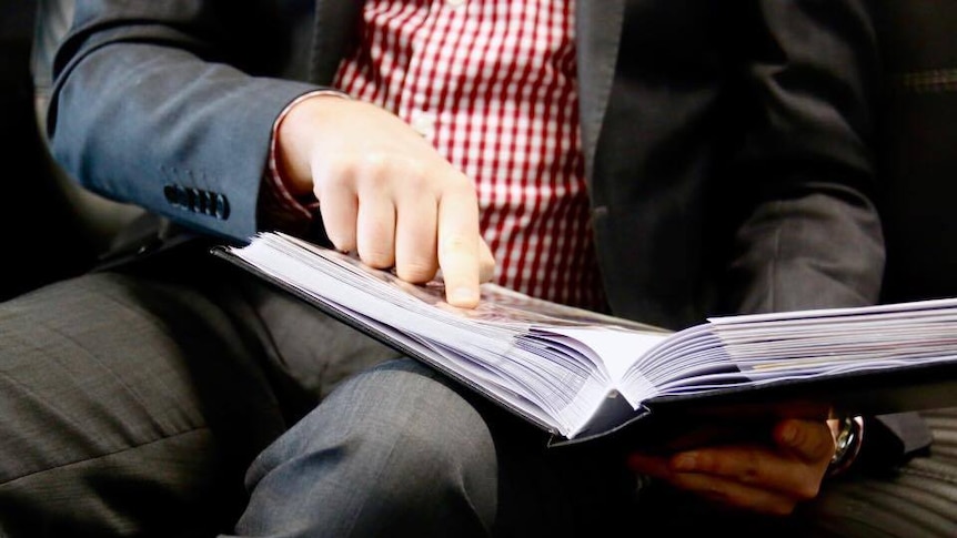 unidentified man looking at open photo album, pointing to photo