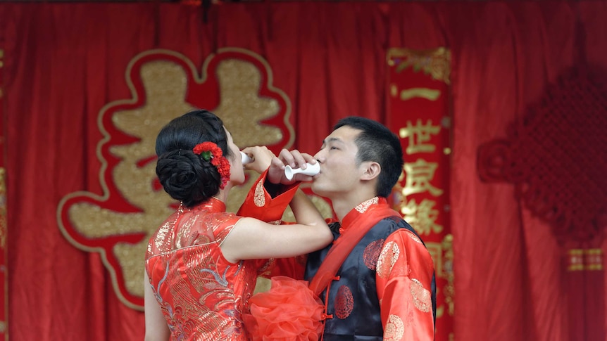 A couple drinks wine with their arms interlinked.