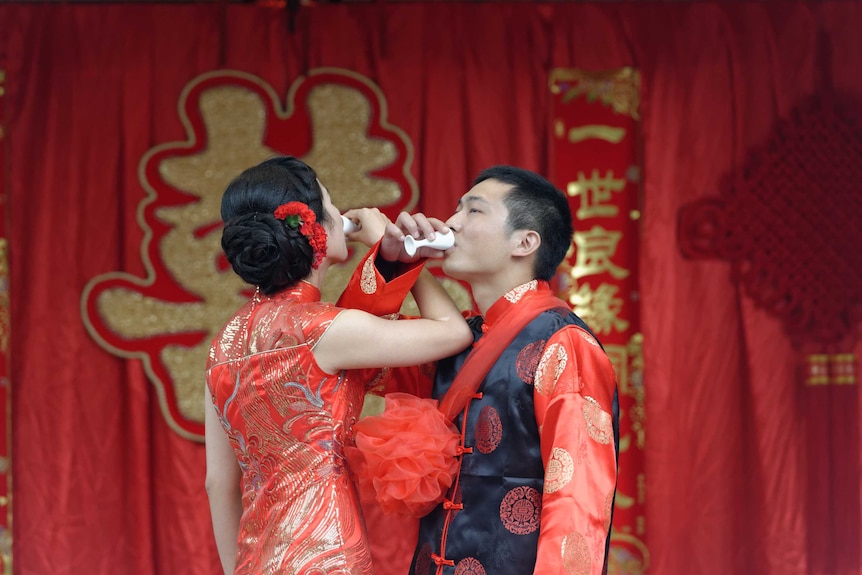 A couple drinks wine with their arms interlinked.