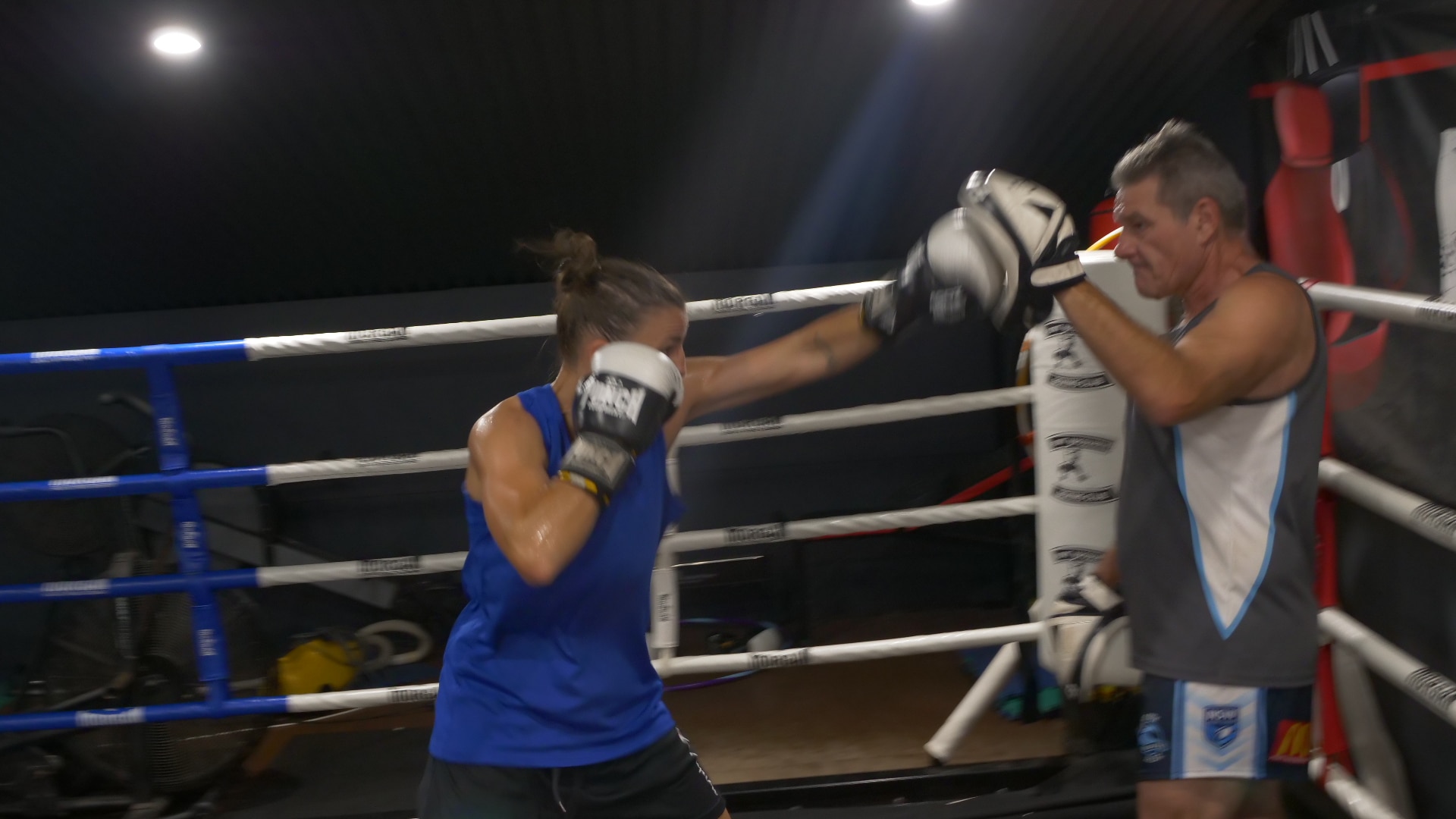 Jess in the ring with her coach punching up to his hand pad, one glove protecting her face.