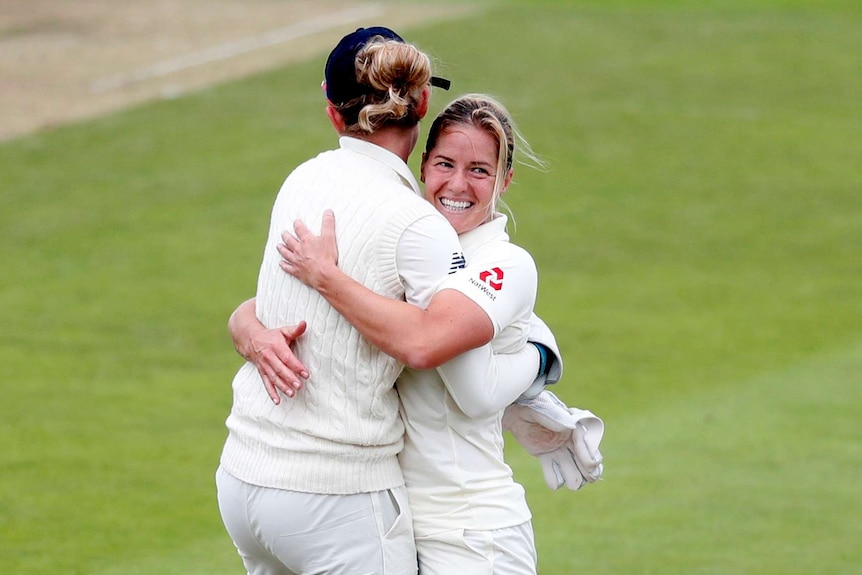 Katherine Brunt smiles and hugs a teammate to celebrate taking a wicket.