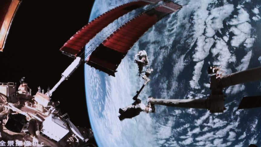 Two astronauts float in the atmosphere with earth seen below. 