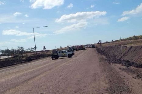 A line of emergency service vehicles on a wide dirt road, outside on a sunny day. 