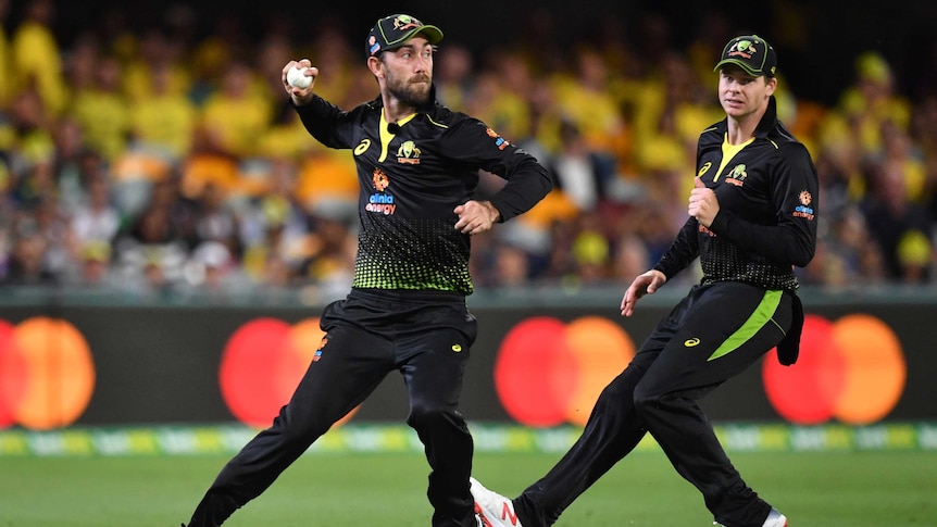An Australian cricketer throws a ball back during a T20 international as a teammate watches on.