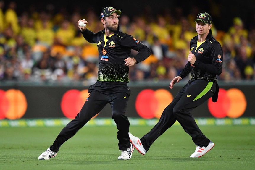 An Australian cricketer throws a ball back during a T20 international as a teammate watches on.