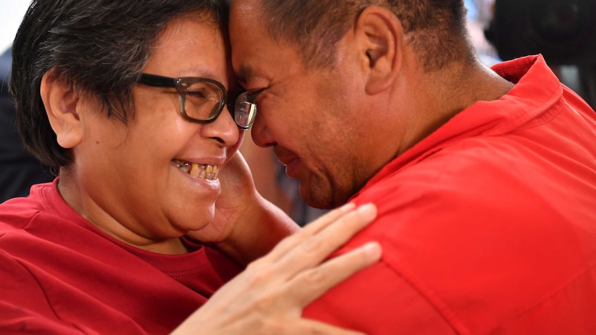 a woman and man in red shirts tearfully embrace each other