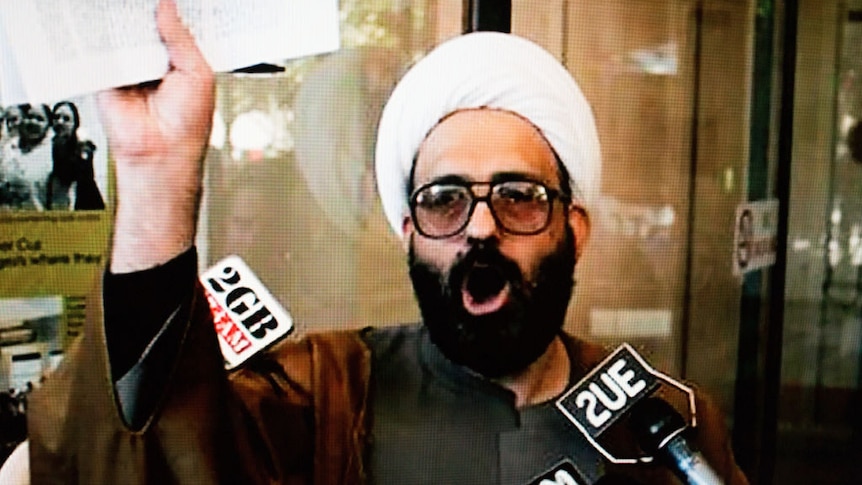 Man in islamic dress holding papers up for TV cameras
