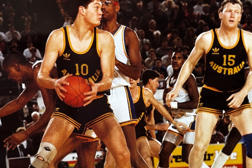 A young man with flaming red hair plays basketball wearing an Australia singlet