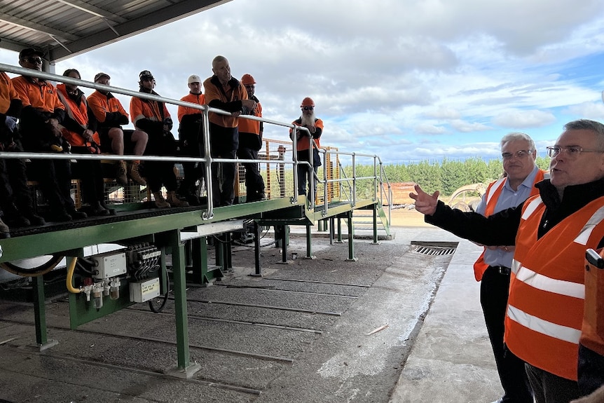 A man in a high vis jacket talking to workers gathered at a Tasmanian sawmill